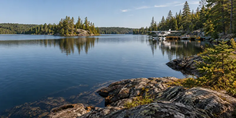 Floatplane moored beside a wooden dock on a pine-lined lake